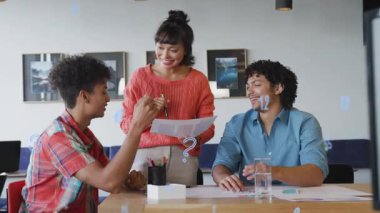 Adam beyaz kutuyu kaldırıyor, kırmızı kazaklı kadını takım çalışmasında çarşafları incelerken gösteriyor. İşbirliği, takım çalışması, iş, tartışma, toplantı, ofis, planlama