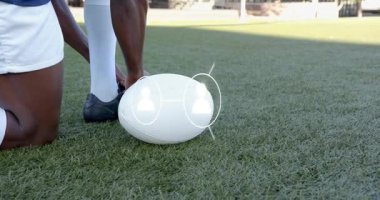 Çimenlikte diz çökmüş erkek sporcu ayakkabıyı ayarlıyor, futbolun yerini oyun için ortaya çıkan ağla dolduruyor. Sporcu, spor, teknoloji, dijital, ağ, iletişim, eğitim