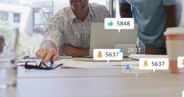 Adam gazetelere işaret ederek pazarlamada sosyal medya simgelerini başlatırken ekip verileri not alıyor. İşbirliği, takım çalışması, dijital, analitik, iş dünyası, beyin fırtınası, modern