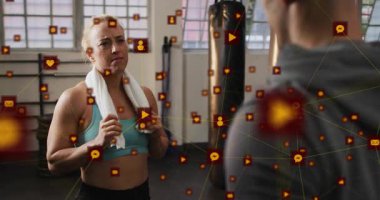 Fitness müşterisi havluyla nefes alıyor ve torba yanında antrenörle konuşuyor. İkonalar büyüme gösteriyor. Eğitim, motivasyon, egzersiz, fitness, dijital, iletişim, aktif