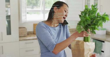 Telefonunu omuz hizasında dengede tutan bir kadın bakkaliye paketleri açıyor, çağrı sırasında yemek hazırlamak için yeşillikleri denetliyor. Yemek pişirme, sağlık, yerli, yaşam tarzı, sağlıklı, iletişim, modern