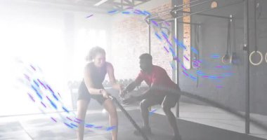 Antrenör, savaş halatlarını tutan ve fitness stüdyosunda alternatif dalga çarpmaları yaratan bir kadına rehberlik ediyor. Dayanıklılık eğitimi, fonksiyonel fitness, atletizm, hareket, kararlılık, egzersiz, spor ortamı