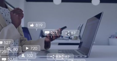 Dijital pazarlamacı akıllı telefonu kaydırıyor ve dizüstü bilgisayarın etrafında yüzen animasyon nişan simgelerini takip ediyor. Teknoloji, katılım, analitik, üretkenlik, profesyonel, dijital, iletişim