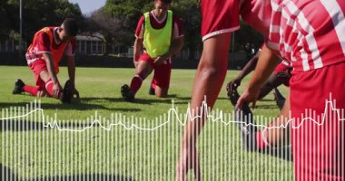 Sahada toplanan erkek futbol oyuncuları bacak esnetme hareketleri yaptıktan sonra hareketli oklar ısınmaya rehberlik ediyor. Atletizm, fitness, takım çalışması, açık hava, aktif giyim, sportmenlik, çeviklik