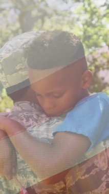 Afro-Amerikan askerinin eve döndükten sonra oğluna sarılmasının ardından ulusal Amerikan bayrağının animasyonu. Dijital bileşim, yıldızlar, çizgili, aile, sevgi, birliktelik, vatanseverlik, ordu, eve dönüş.