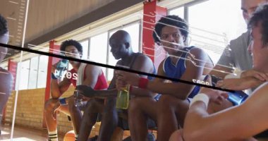 Basketbol oyuncuları bir sonraki oyundan önce veri zaman çizelgesini izleyip kaydırma ve hidratlaştırma yapıyorlar. Takım arkadaşları, yoldaşlık, hidrasyon, sporcular, dijital arayüz, fitness, takım çalışması.