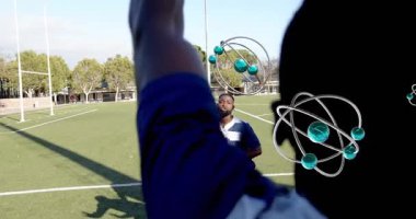 Mavili oyuncu ragbi topunu fırlatıyor. Yörüngesinde AR küreleri olan takım arkadaşını kaldırmaya doğru. Atletizm, takım çalışması, teknoloji, rekabet, fitness, spor, yenilik