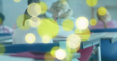 Masasında pembe kalemle yazan öğrenci sarı dairelere tepki veriyor ve kameraya doğru dönüyor. Çocuklar, eğitim, sınıf, öğrenme, takım çalışması, neşeli, enerjik