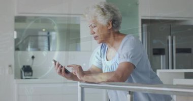 Üst düzey bir kadın akıllı telefon yetiştiriyor ve ev mutfağında teknoloji incelemeleri yapıyor. Dijital, modern, yaşam tarzı, teknoloji, sağlık, iletişim, kıdemli