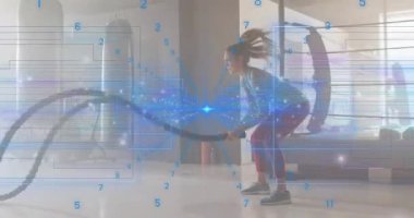 Mavi veri renklendirme ölçümlerini üst üste koyarken, kadın egzersizi savaş halatı dalgalarını başlatıyor. Zindelik, güç, dayanıklılık, spor salonu, eğitim, sağlık, hareket