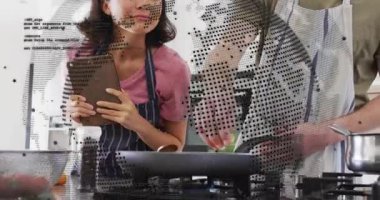 Kadın, yemek demosu sırasında tablet tarifi, erkeğin baharat kullanması ve ocağın üstünde yemek çevirmesi. Aşçılık, takım çalışması, modern, yerli, aşçılık, işbirliği, hazırlık