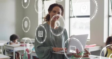 Öğretmenin sınıfa girmesi, dizüstü bilgisayarda yazması öğrenciler arasında yüzen eğitim simgeleri oluşturması. Eğitim, dijital, yenilik, öğrenme, sınıf, teknoloji, pedagoji