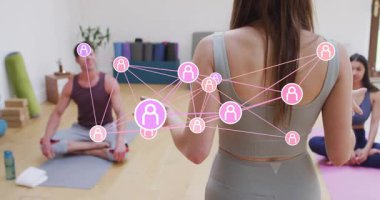 Yoga eğitmeni elini kaldırıyor ve öğrenci odağı için paspasların üzerine bağlanan kullanıcı simgesi düğümlerine rehberlik ediyor. Farkındalık, bağlantı, dijital, sağlık, etkileşimli, uyum, hareket