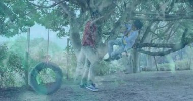 Muhafız, çocuğu dal üzerinde sabit tutuyor ve hareketli momentum çubuğuyla aile eğlencesinde salıncak sallıyor. Aileler, açık hava oyunları, çocukluk, bağ, doğa, neşe, macera