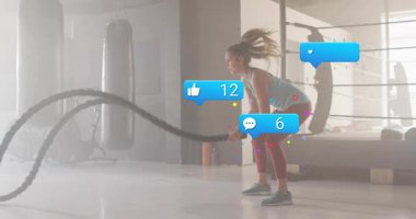 Spor salonuna giren kadın sporcu savaş halatlarını tutuyor dalgalar yaratıyor, hareketli sosyal sayıları arttırıyor. Fitness, dayanıklılık, kardiyo, antrenman, spor salonu, hareket