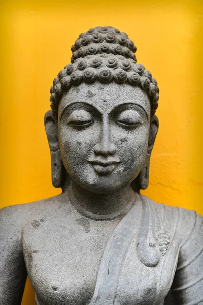 Close up Buddha Face Statue Isolated On Yellow French Colony Wall Background, Granite Buddha Statue Portrait.