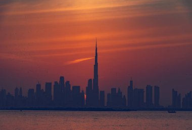 Dubai 'nin güzel gün batımı manzarası Burj Halife silueti ile birlikte. Panoramik şehir manzarası seyahat, başyazı veya ticari kullanım için mükemmel. Burç Halife canlı turuncu bir gökyüzüne karşı siluetlendi.