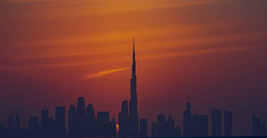 Dubai silueti üzerinde çarpıcı bir günbatımı. İkonik Burj Halife silueti var. Bir kuş sürüsü zarif bir şekilde kulenin üzerinde uçuyor. Seyahat, yazı işleri ve ticari kullanım için ideal.