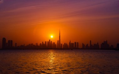Dubai ufuk çizgisinin güzel gün batımı manzarası. Dubai Creek Limanı 'ndan çekilen Burj Halife silueti. Seyahat, yazı işleri veya ticari kullanım için mükemmel çarpıcı bir kentsel manzara.