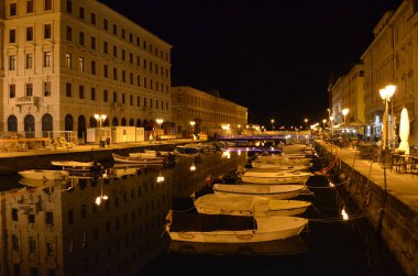 Trieste, İtalya, Büyük Kanal 'ın gece manzarası demirli tekneleri, tarihi mimarisi ve arka planda yanan Sant' Antonio Nuovo kilisesi.