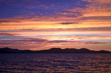 Hırvatistan 'ın Zadar kenti, Adriyatik Denizi üzerinde canlı günbatımı renkleri, parlayan bulutlar ve siluetlerle alacakaranlıkta sersemletici deniz manzarası