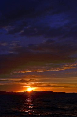 Hırvatistan 'ın Zadar kenti, Adriyatik Denizi üzerinde pırıl pırıl su ve kıyı tepelerinin uzak siluetleriyle parıldayan altın gün batımı