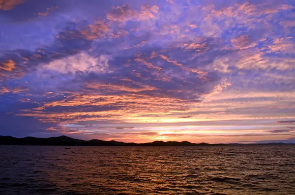 Hırvatistan 'ın Zadar kenti, Adriyatik Denizi üzerinde canlı günbatımı renkleri, parlayan bulutlar ve siluetlerle alacakaranlıkta sersemletici deniz manzarası