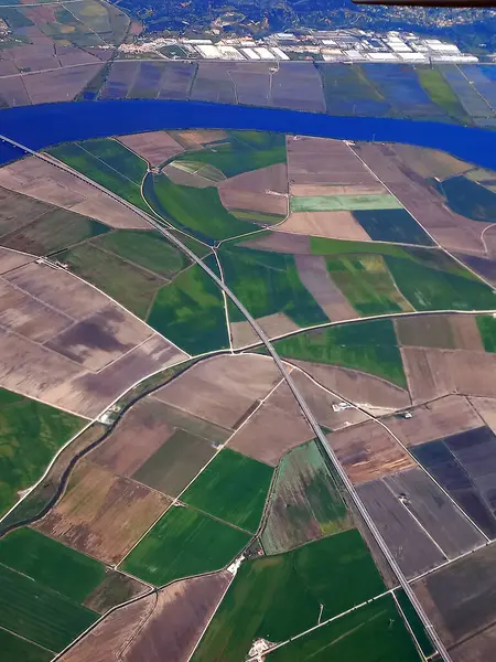 Nehir kenarındaki yollar ve su yolları tarafından kesilen yeşil ve kahverengiye benzer çeşitli tarımsal arazilerin canlı hava görüntüsü.