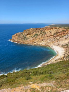 Sesimbra Portekiz 'deki Cape Espichel sahil şeridinin panoramik manzarasında engebeli uçurumlar turkuaz okyanus ve güneşli bir günde sakin bir çakıl taşı plajı var.