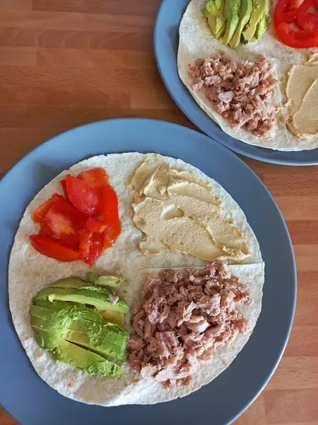 Taze tortilla ambalajı dilimlenmiş avokado ton balığı domatesi ve besleyici dengeli bir yemek için humus da dahil olmak üzere ayrı malzemelerle açıldı.