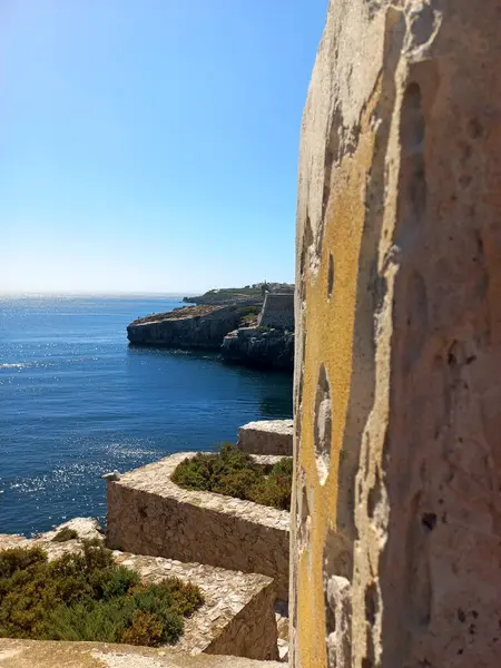 Penis, Portekiz. 21 Temmuz 2024 Engebeli kireçtaşı kale duvarları Peniche 'deki açık mavi Atlantik Okyanusu' na bakan parlak öğle güneşi altında