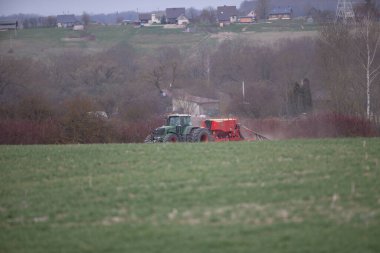 Yüksek tekerlekli traktör genç buğdayda gübre yapıyor. Etrafa saçılmış sprey kimyasalların kullanımı. Üzerinde sprey cihazı olan bir traktör. Gübre olarak kullanılıyor. 04 19 2022