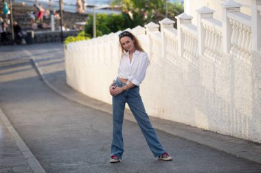 Sokakta poz veren mavi kotlu, modaya uygun tişörtlü, modern, çekici genç bir kadın. Güzel Avrupalı kız dışarıda bir yaz gününün tadını çıkarıyor..