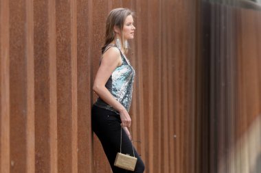 A beautiful young woman poses outside near a rusty fence
