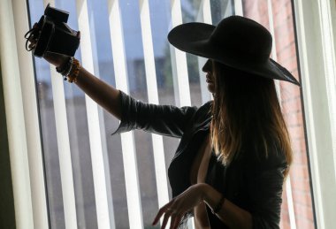 Beautiful young woman taking selfie with instant camer