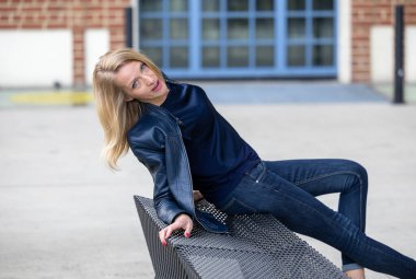 Deri ceketli, mavi kotlu, terk edilmiş bir fabrikada şehvetli pozlar veren bir model.