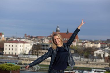 Mavi ceketli, koyu renk gömlekli ve kot pantolonlu güzel bir kadın Krakow şehrinin arka planında poz veriyor.