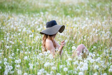 Karahindiba otlağında şapkası olan güzel genç bir kadın.