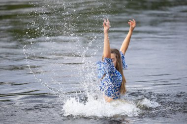 Genç bir kız sıcak bir yaz akşamında nehir suyuna su sıçratıyor.