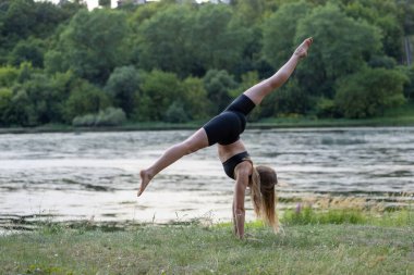 Güzel genç bir kadın nehir kenarında yoga yapıyor.