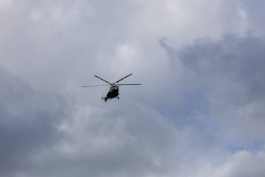 Mavi gökyüzünde bulutlarla uçan bir helikopterin silüeti.