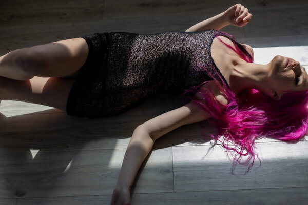 Young beautiful girl with pink hair in black lingerie on the floor
