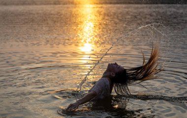 Genç güzel kız altın gün batımından önce gölde banyo yapıyor.