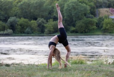 Güzel genç bir kadın nehir kenarında yoga yapıyor.