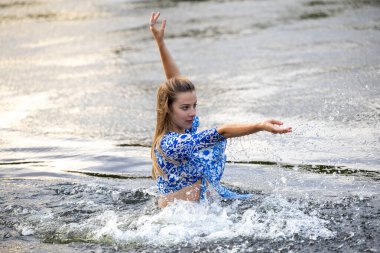 Genç bir kız sıcak bir yaz akşamında nehir suyuna su sıçratıyor.