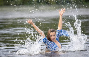 Genç bir kız sıcak bir yaz akşamında nehir suyuna su sıçratıyor.