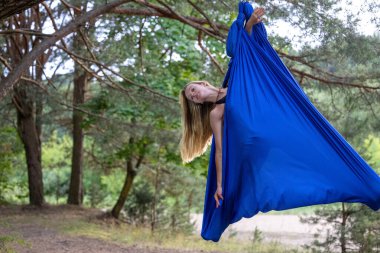 Genç bir kadın parkta havadan ipekle yerçekimi yogası yapıyor..