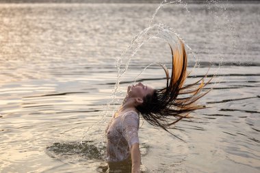 Genç güzel kız altın gün batımından önce gölde banyo yapıyor.