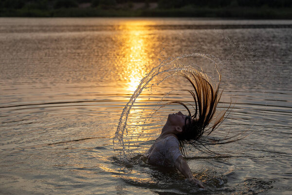Young pretty girl relaxing bath in lake before golden sunset