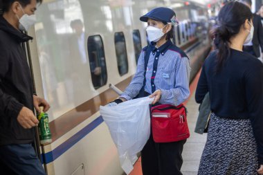 Japonya 'da bir tren istasyonunda çöp toplayan bir kadın, tren vagonunun yanında.